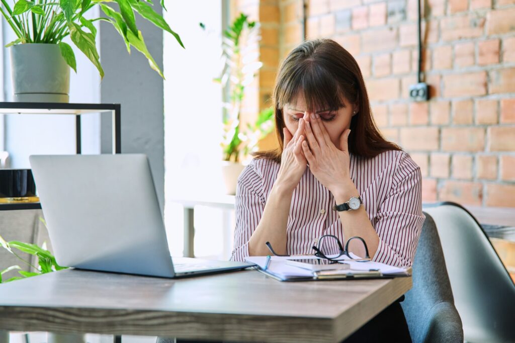 Mature tired worried tense woman at workplace experiencing stress headache