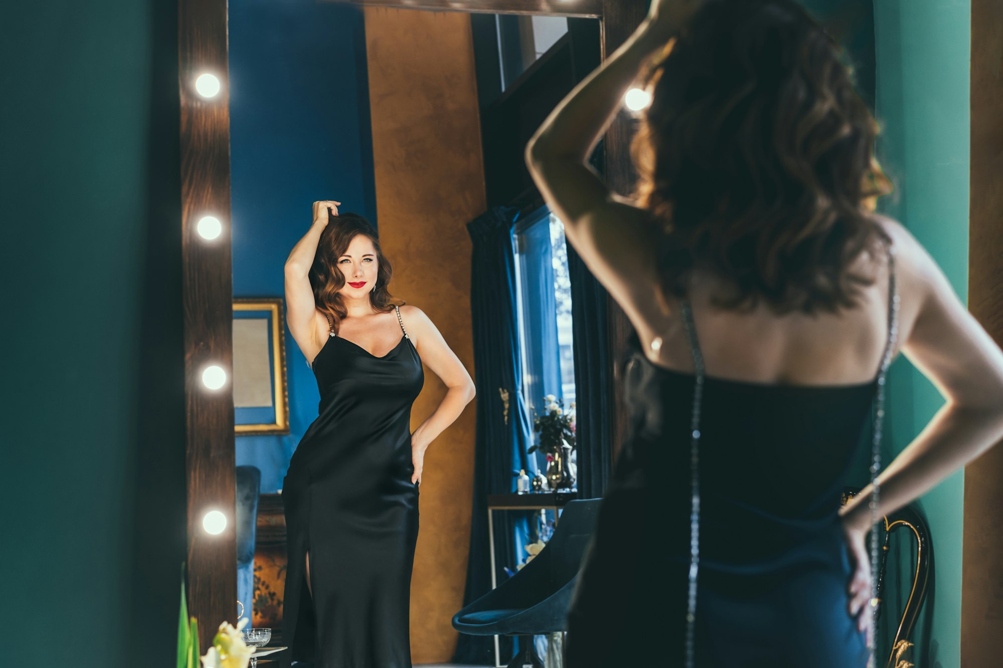 Sexy young woman in elegant cocktail silk black dress dancing and posing in mirror reflection